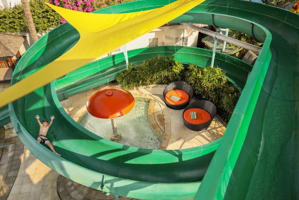 Ūdens slidkalniņš ar bērnu, kas bauda slidināšanos, un atpūtas zonas ar krēsliem, izsistot prieka un atpūtas atmosfēru.