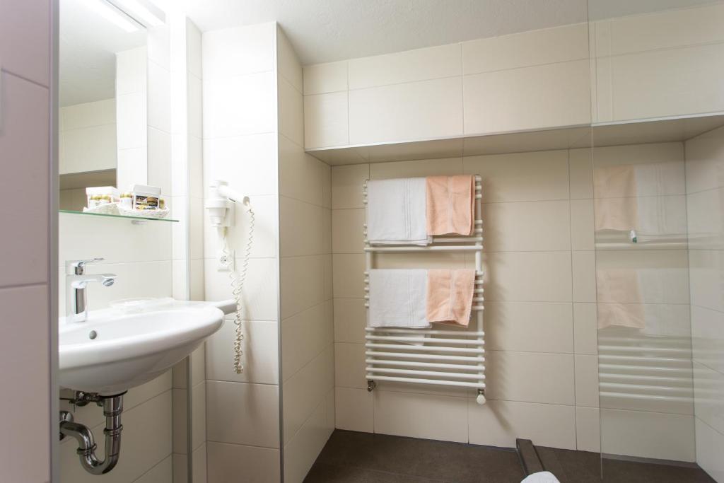 Mūsdienīga vannas istaba ar gaišām flīzēm, izlietni un dvieļu žāvētāju. Interjers ir minimālistisks un funkcionāls.