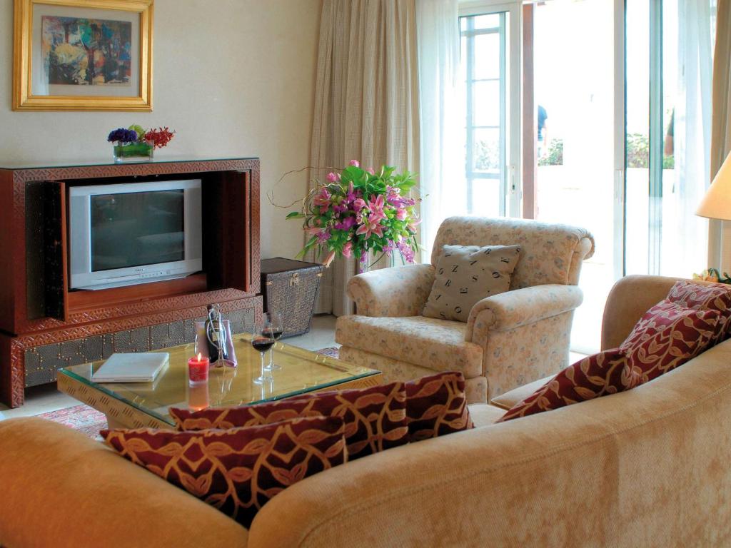 Mūsdienīgs viesistabas interjers ar dīvānu, krēslu un televizoru. Uz galda ir vīns un svecīte, bet logi sniedz gaismu un skatu uz dārzu.