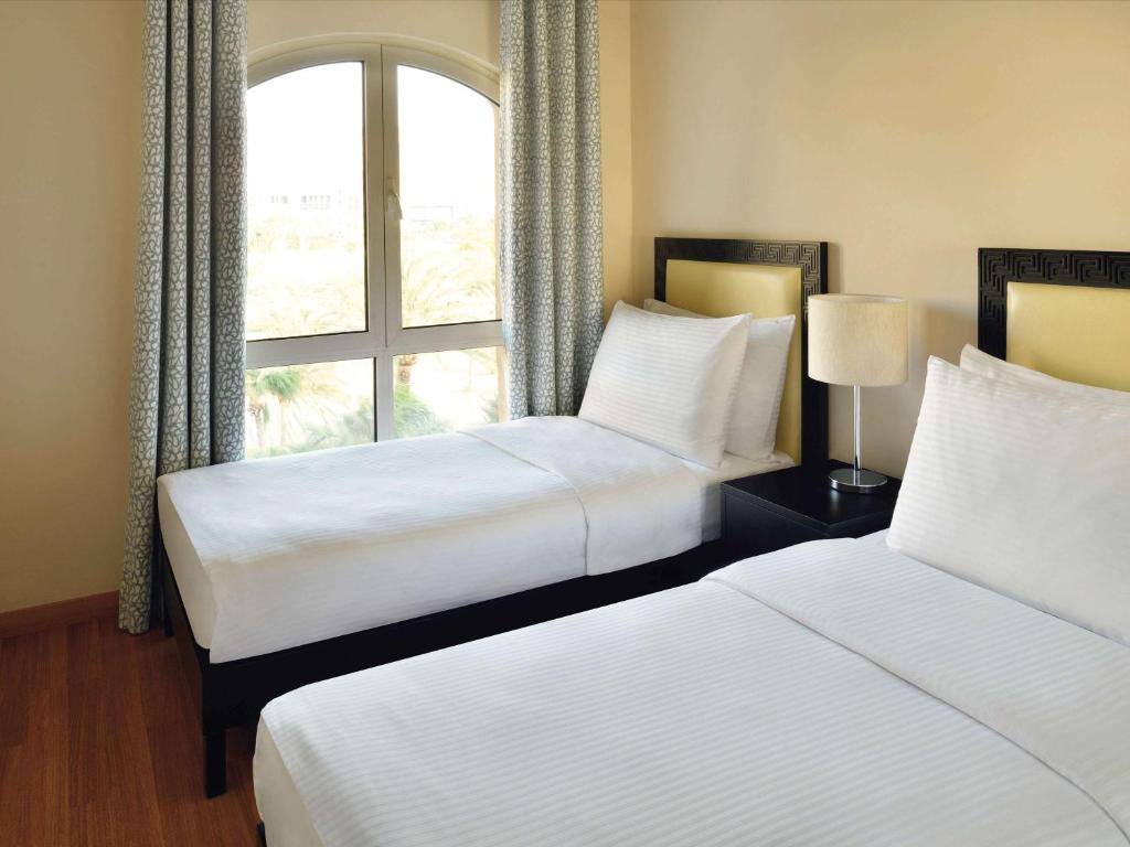 Mūsdienīgs guļamistabas interjers ar divām gultām, logu ar skatu uz dārzu un gaismas avotu uz naktsgaldiņa.