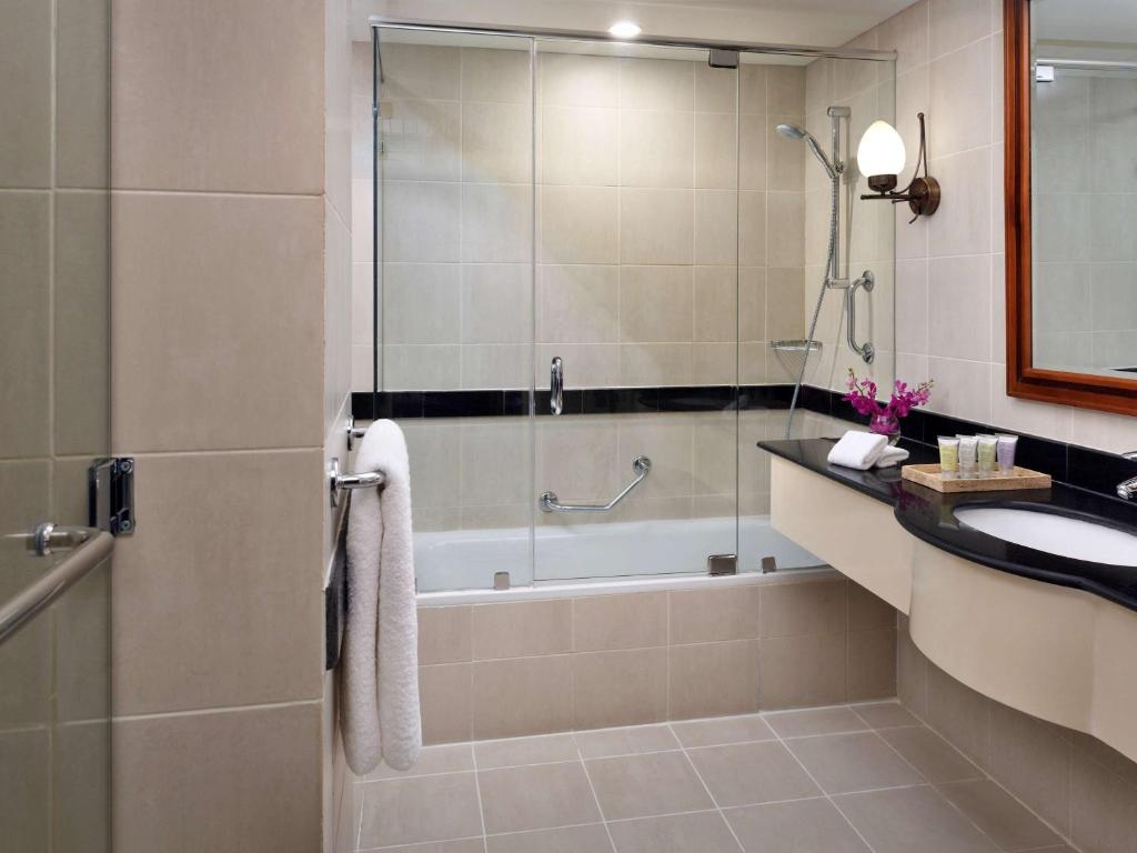 Mūsdienīgs vannas istabas interjers ar stikla dušas kabīni, vannu un melnu marmora izlietni, papildināts ar dekoratīviem elementiem un higiēnas piederumiem.