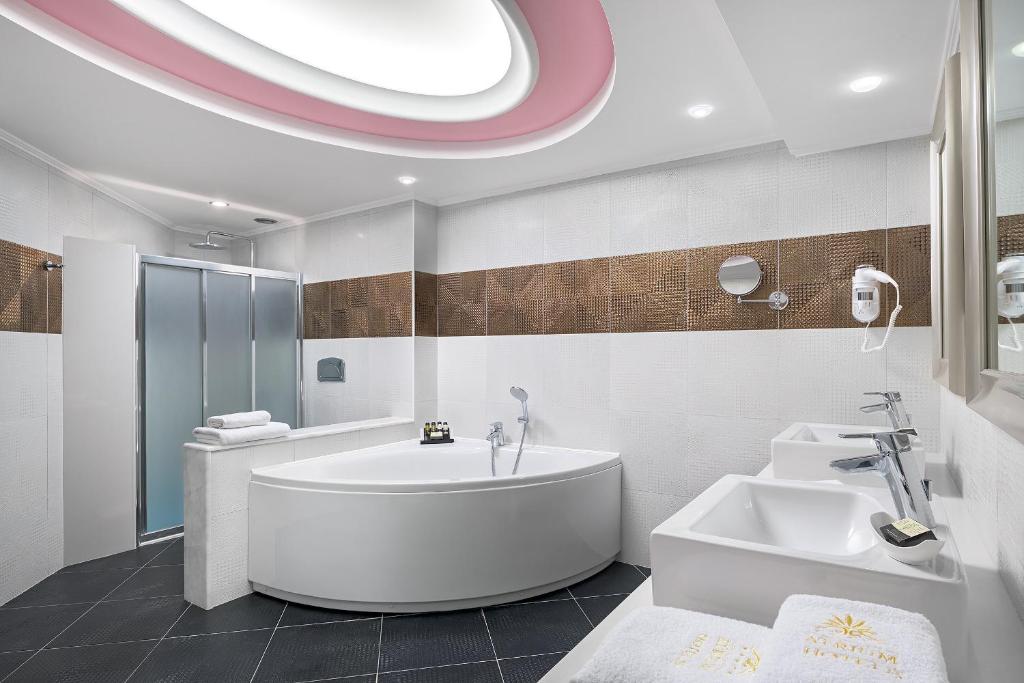Mūsdienīgs vannas istabas interjers ar elegantu apgaismojumu, ovālu vannu un dušu, kas izveidota ar pelēko un brūno flīžu kombināciju.