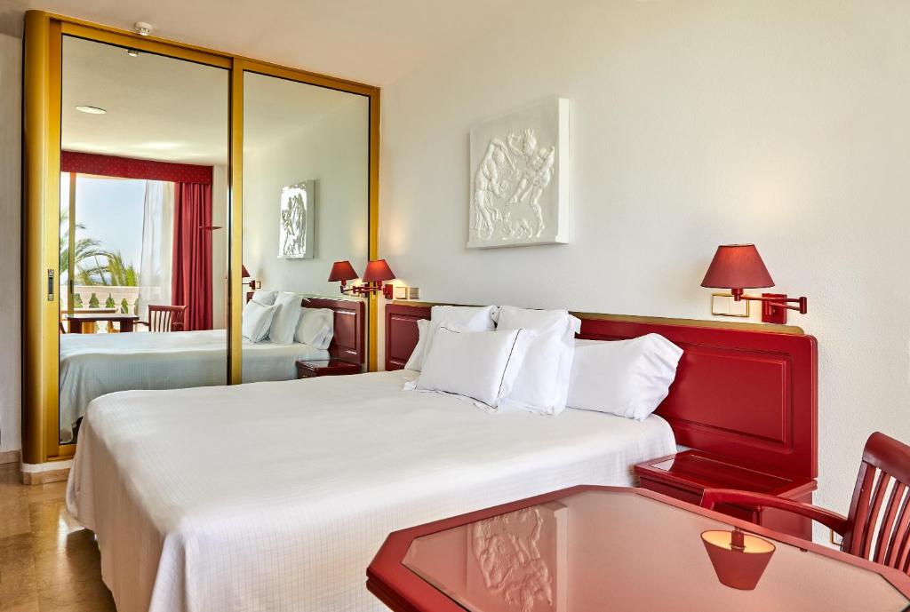 Mūsdienīgs viesnīcas numurs ar divguļamo gultu, sarkanu galdu un atpūtas krēslu, kas piedāvā skatu uz ārpusi caur logu ar sarkanu aizkaru. Numurā ir spogulis un mākslas darbs uz sienas.