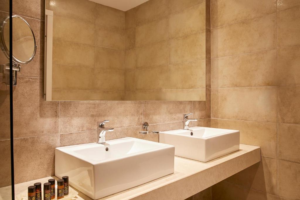 Moderns vannas istabas interjers ar diviem kvadrātveida izlietnēm un lielu spoguli. Sienas ir klātas ar smilškrāsas flīzēm, radot mājīgu atmosfēru.