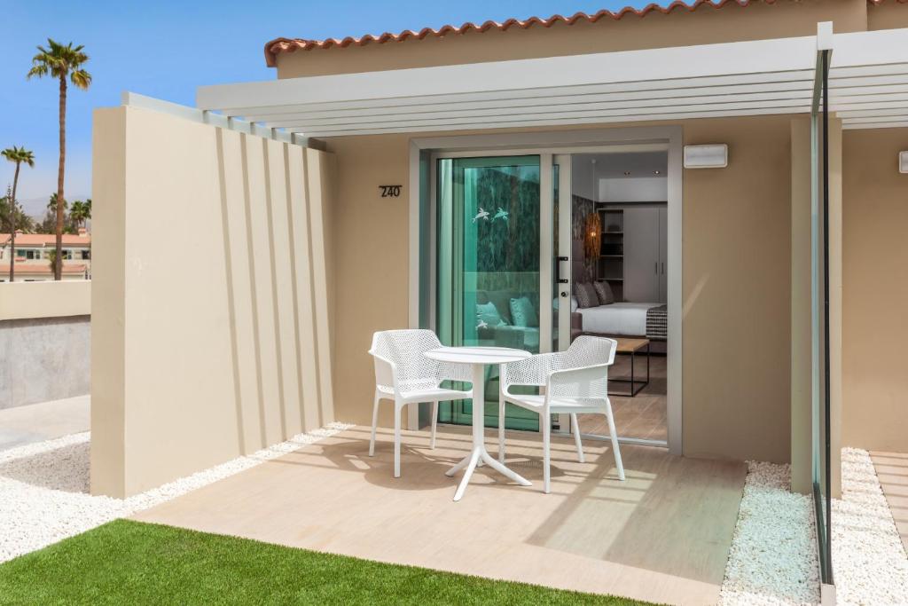 Mūsdienīgs viesnīcas numura balkons ar galdu un krēsliem, apzaļumotā teritorijā. Fons ar palmām un plašu skatu uz iekštelpu telpu.