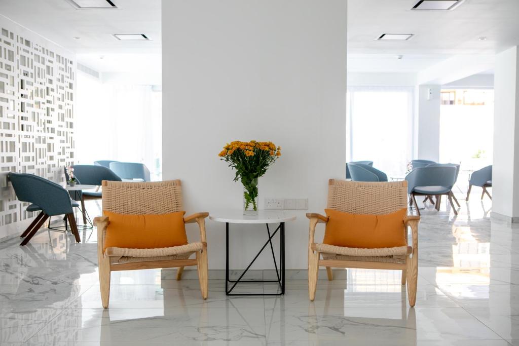 Mūsdienīgs interjers ar divām krēslām un baltu galdiņu, uz kura atrodas ziedu pušķis. Fonā redzami gaiši zili krēsli un eleganta apdare.