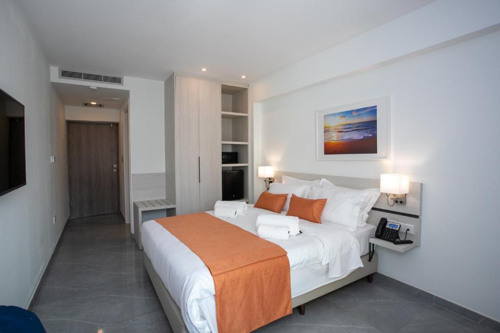 Mūsdienīga viesnīcas numura iekārtojums ar divguļamo gultu, siltām oranžām akcentiem un modernām mēbelēm. Numurā ir televizors, telefons un skats uz mākslas darbu pie sienas.