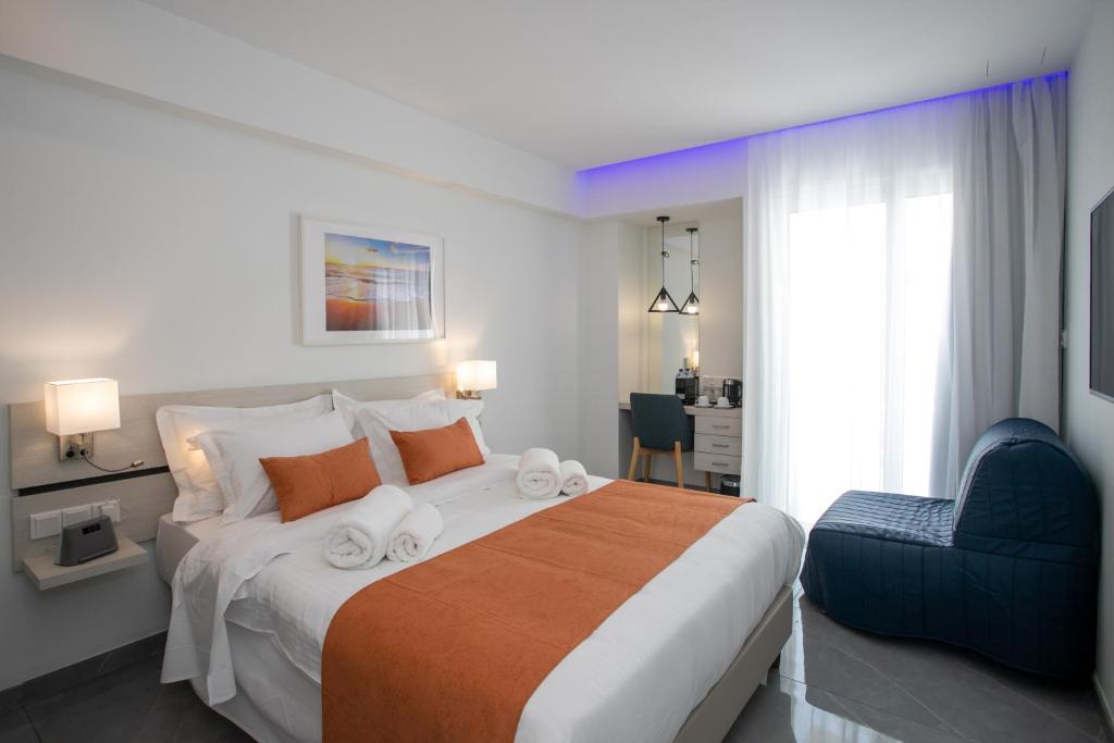 Mūsdienīgas viesnīcas numurs ar ērtiem gultas piederumiem, oranžu segu un atpūtas krēslu, kas nodrošina relaksējošu atmosfēru. Gaisma un interjers rada mājīgu noskaņu.
