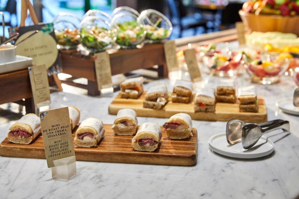 Mini sviestmaizes ar ceptu liellopu gaļu un siera mērci, izkārtotas uz galda, apkārt salāti un augļu deserts.