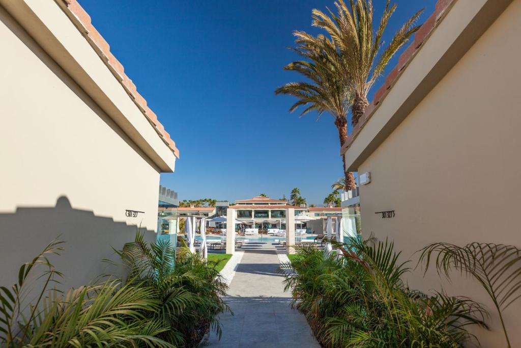 Mūsdienīgs kūrorts ar palmām un peldbaseinu, redzams caur šauru ieeju, kas ieskauj zaļumi. Ideāla vieta atpūtai un relaksācijai.