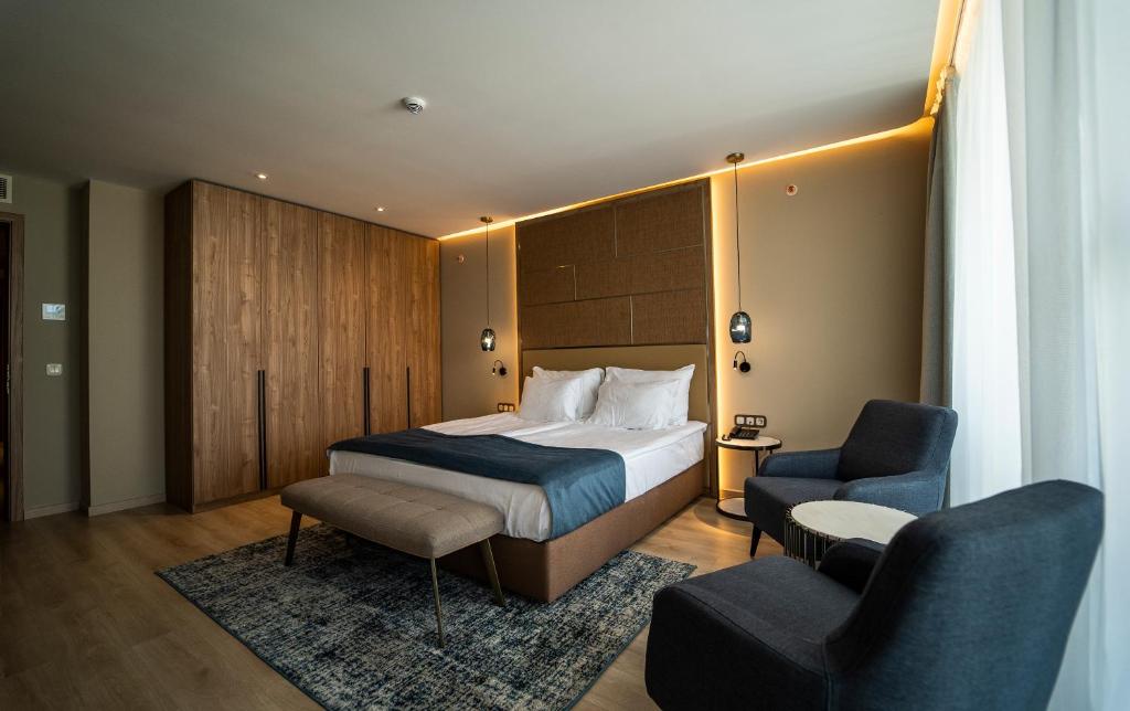 Mūsdienīga viesnīcas numura interjers ar divguļamo gultu, ērtām krēsliem un koka skapjiem. Telpas apgaismojums un dizains rada relaksējošu atmosfēru.