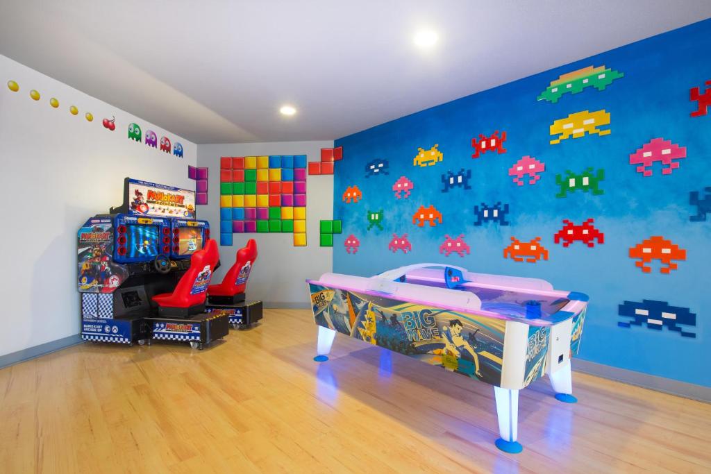 Spēļu telpa ar retro spēļu automātiem un krāsainām grafiti uz sienām, radot jautru un dinamisku atmosfēru. Centrā ir gaisa hokeja galds un Mario Kart spēļu automāti.
