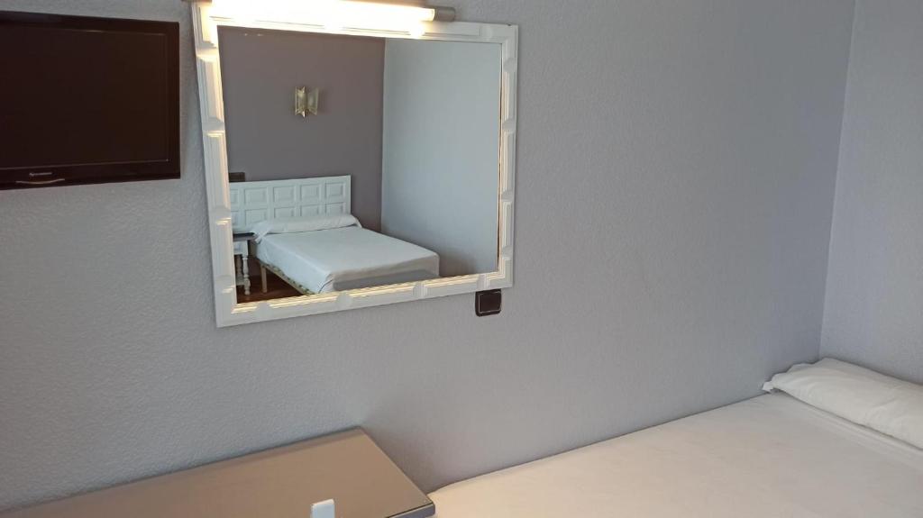 Mūsdienīga guļamistaba ar pelēkām sienām, gultu un spoguli. Interjerā ir televizors un minimāla mēbeļu izvēle, radot tīru un vienkāršu atmosfēru.