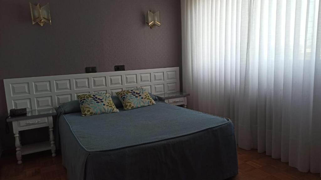 Mūsdienīgs guļamistabas interjers ar gultu, spilveniem un gaismas avotiem. Lielas logu aizkari nodrošina dabisko apgaismojumu.