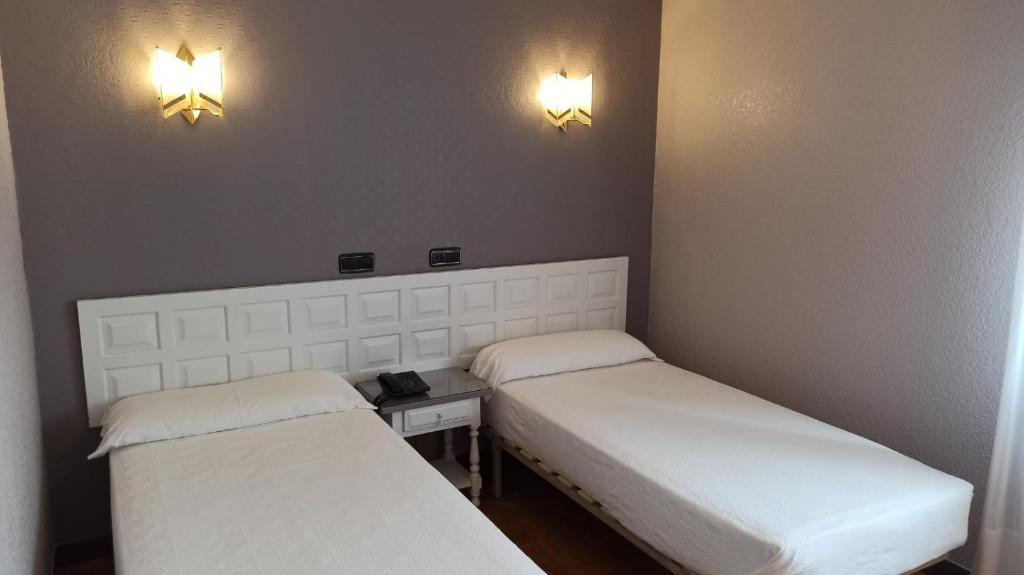 Gaiša guļamistaba ar divām atsevišķām gultām, baltu galvgali un pie sienas piestiprinātām lampām, radot mierīgu atmosfēru. Ideāla vieta atpūtai un relaksācijai.