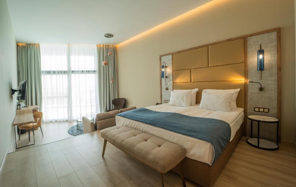 Mūsdienīga viesnīcas istaba ar divguļamo gultu, dīvānu un koka mēbelēm. Lieli logi nodrošina daudz gaismas un skatu uz ārpusi.