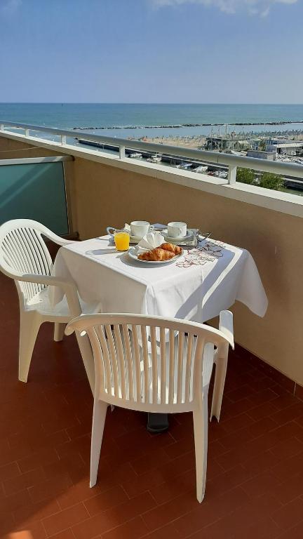 Balkona galds ar brokastīm, kurā redzams kruasāns, kafija un apelsīnu sula, ar skatu uz jūru un pludmali.