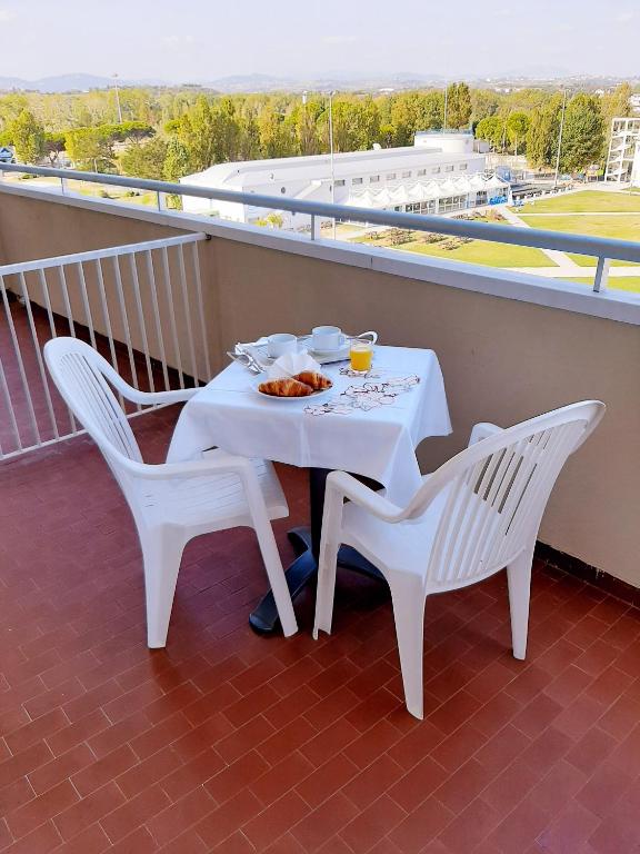 Balkons ar galdu un krēsliem, uz kura ir brokastu galds ar krēmiem, kruasāniem un sulu, ar skatu uz zaļo laukumu.