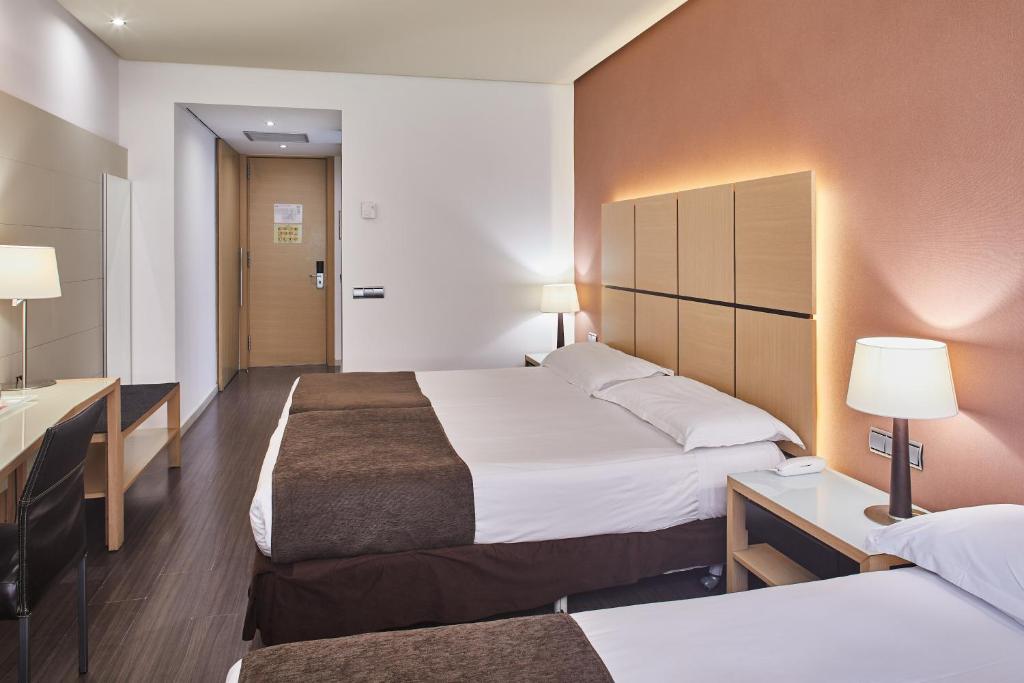 Mūsdienīga viesnīcas numura iekārtojums ar divām gultām, galdu un spoguli, apgaismots ar siltu gaismu. Interjers ir elegants un funkcionāls, ar koka grīdu un neitrālām krāsām.