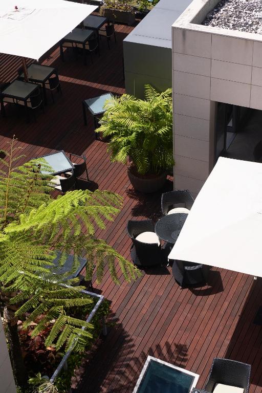 Dārza terase ar galds un krēsliem zem saulessargiem, ieskauta zaļumiem un dekoratīvām augu kompozīcijām. Ideāla vieta relaksācijai un atpūtai.