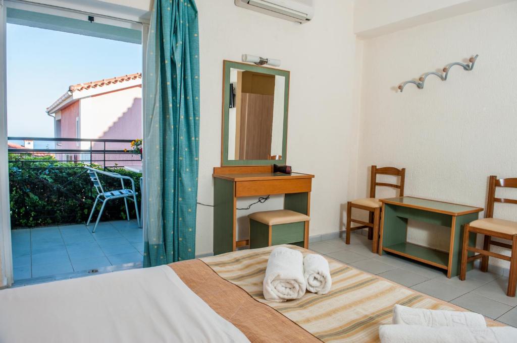 Svaigas un gaišas viesnīcas istabas interjers ar balkonu, skatu uz dārzu un jūru. Telpā ir gulta, spogulis un koka mēbeles.