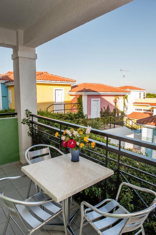 Balkons ar galdiņu un krēsliem, uz kura atrodas ziedu pušķis, skats uz krāsainām mājām un zaļo dārzu.
