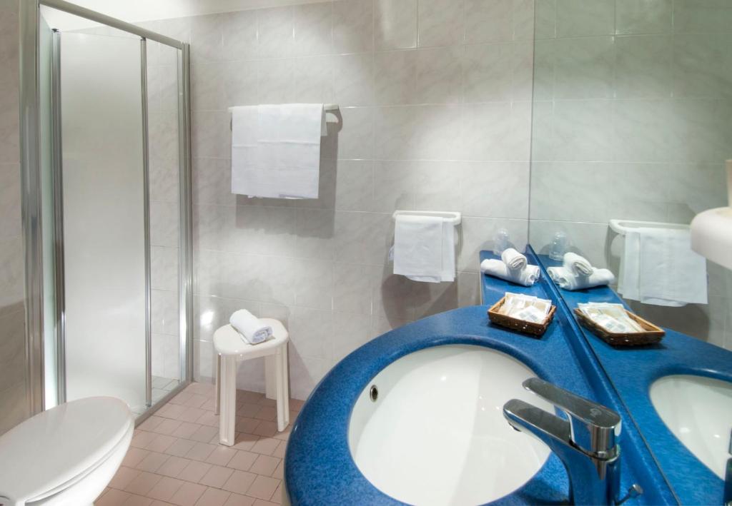 Mūsdienīgs vannas istabas interjers ar apaļu izlietni, dušas kabīni un plauktiem, kas satur dvieļus un higiēnas piederumus.