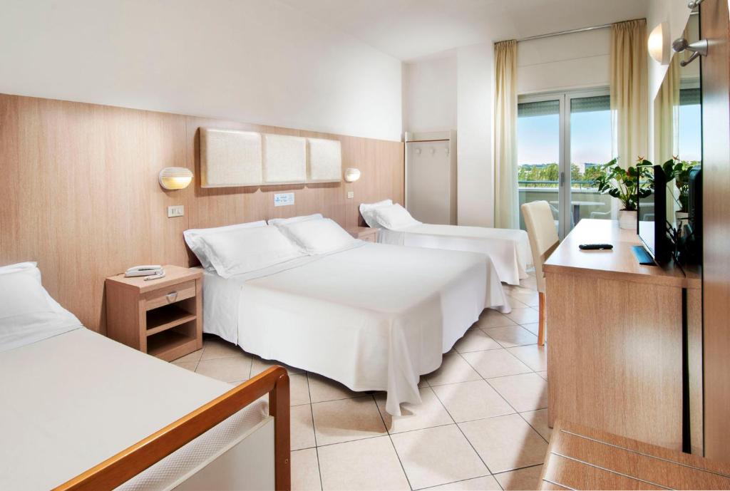 Mūsdienīgs viesnīcas numurs ar trīs gultām un koka mēbelēm, kuru rotā neitrālas krāsas un dabiskā apgaismojuma elementi. Gultas ir pārklātas ar baltām sega, un istabā ir televizors un augi.