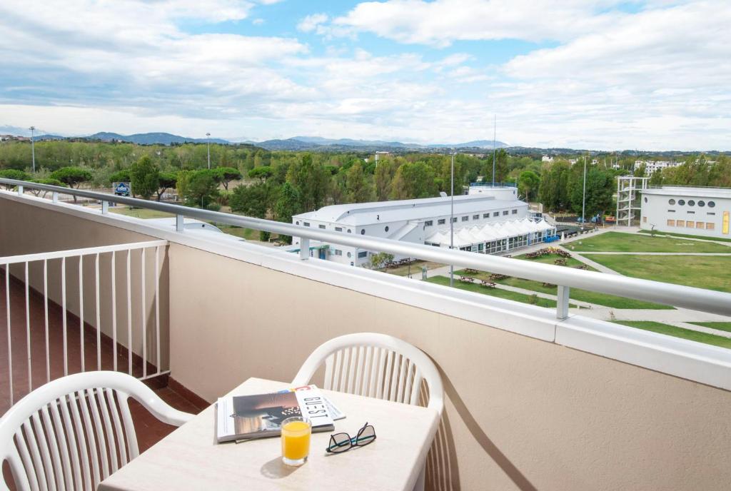 Skats no balkona ar galdu un krēslu, uz kura atrodas grāmata un dzērienu glāze, fonā redzamas zaļās ainavas un kalni.