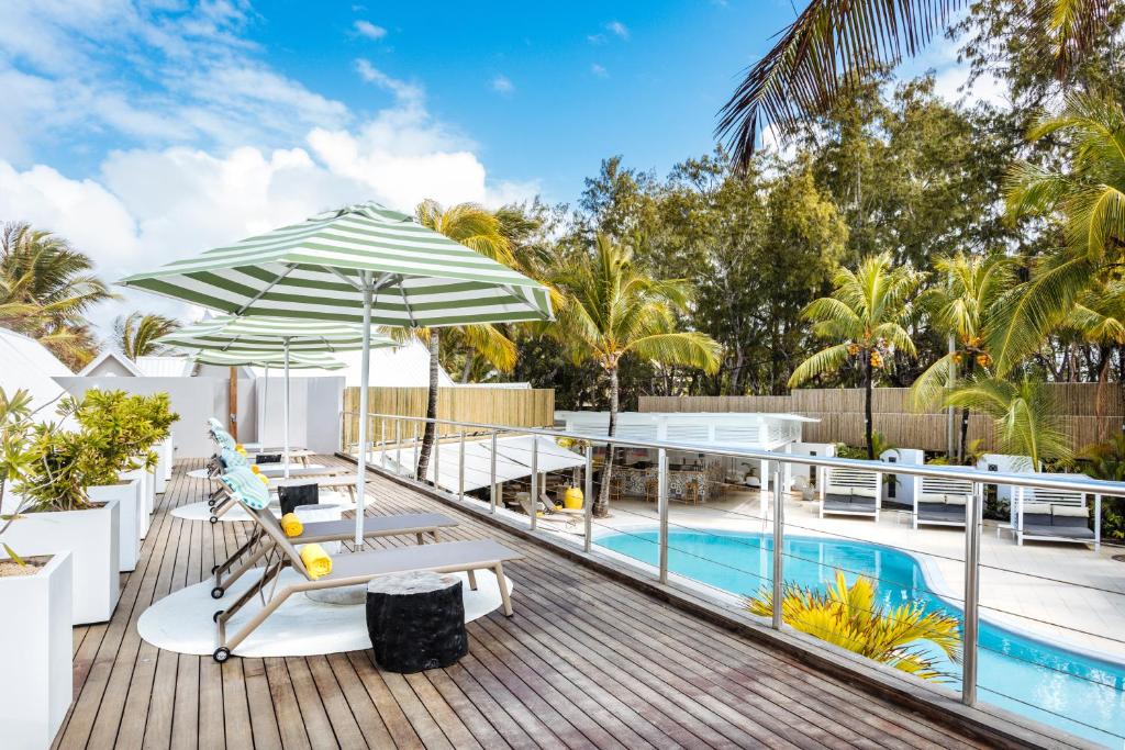 Saulaina atpūtas zona ar baseinu, sauļošanās krēsliem un zaļiem lietussargiem, ko ieskauj palmām un augiem. Ideāla vieta relaksācijai un atpūtai.