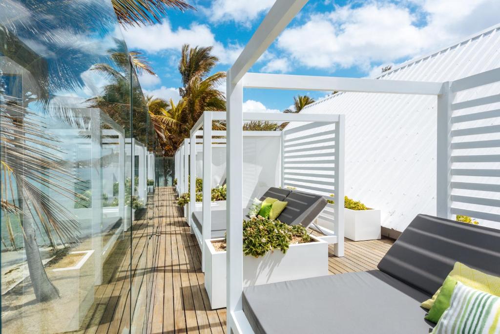 Mūsdienīgs atpūtas laukums ar komfortablām guļvietām, kas izvietotas zem baltiem nojumes rāmjiem, blakus palmām un jūrai. Skaista ainava ar saulainu debesu fonu.