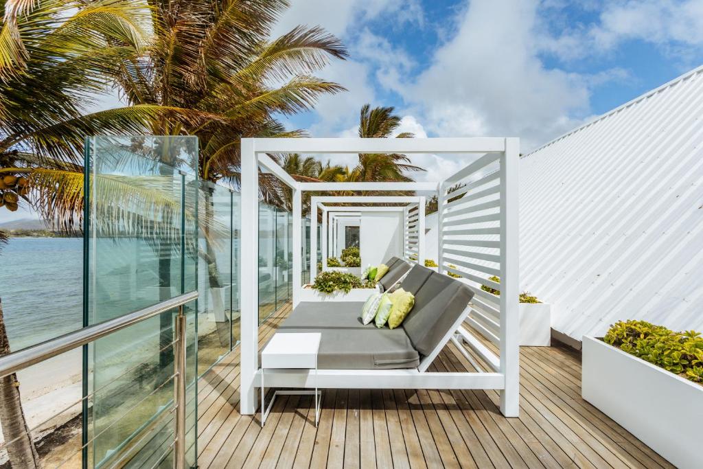 Mūsdienīga atpūtas zona ar baltām koka lapenēm un ērtām gultām, kas atrodas pie jūras, ieskauta palmām un zilo debesu fonā.