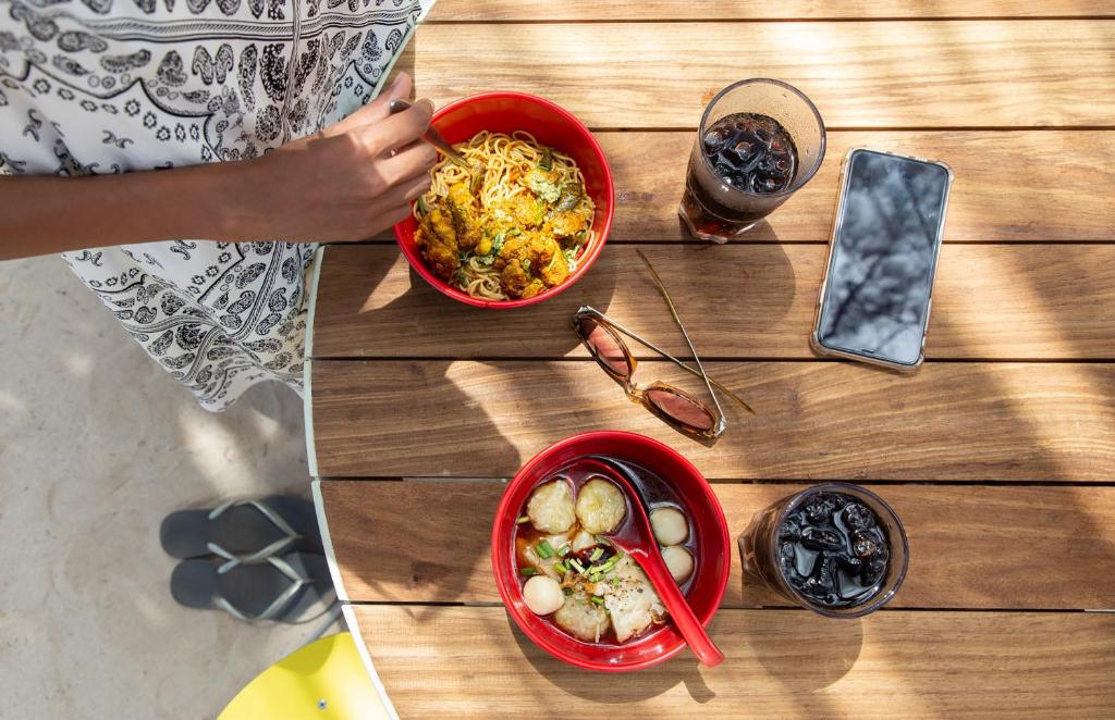 Svaigas maltītes, kas pasniegtas sarkanos traukos, ar nūdeles un zupu, kopā ar dzērieniem un telefonu uz koka galda.