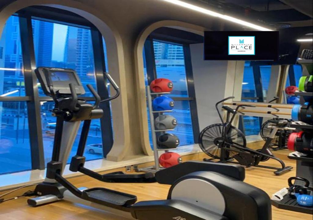 Mūsdienīga sporta zāle ar dažādām trenažieriem un sporta inventāru, logi piedāvā skatu uz pilsētu. Uz ekrāna redzams logotips "Millennium Place Marina".
