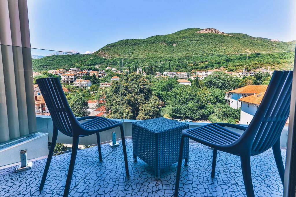 Balkons ar divām krēslām un zilu galdiņu, skats uz kalniem un pilsētas ainavu.
