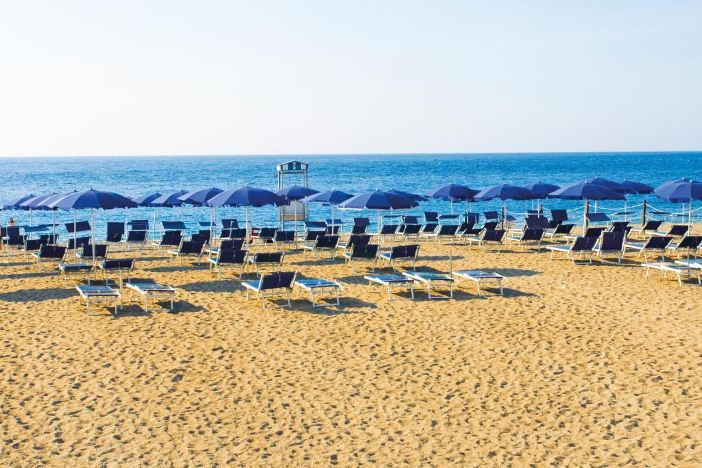 Pludmale ar saulessargiem un atpūtas krēsliem, kas izvietoti smiltīs pie jūras. Kluss un saulains skats uz okeānu.