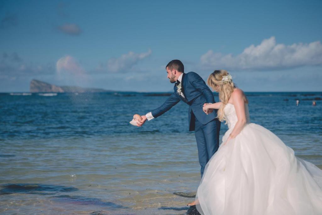 Jaunlaulātie stāv pie pludmales, izmetot ziedus jūrā, fona ir skaista jūra un debesu zilā krāsa.