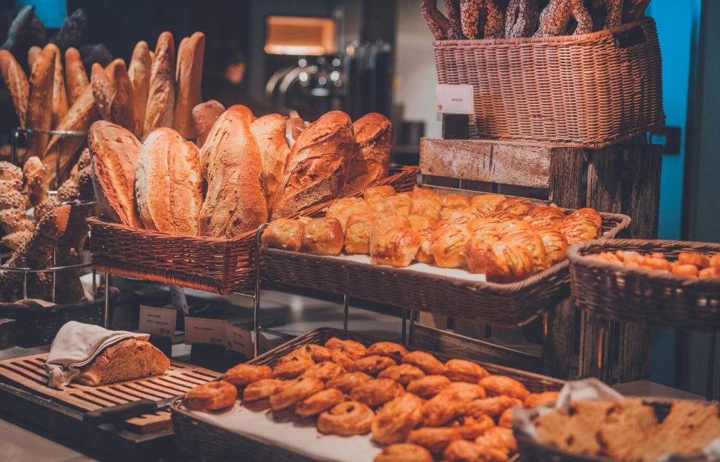 Maizes un konditorejas izstrādājumu stends ar dažādām maizēm un saldumiem, kas izvietoti grozos un uz koka plauktiem.