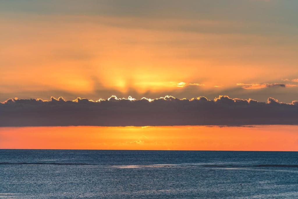 Saulriets virs mierīgas jūras, ar krāsainām mākoņu joslām. Dabas skaistums un mierīgs skats.