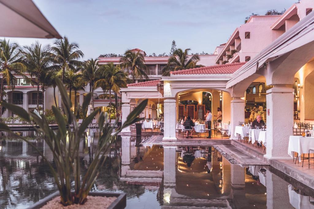 Eleganta viesnīca ar restorānu, kas atrodas pie baseina, apzaļumota ar palmām. Rāmā atmosfērā viesi bauda vakariņas, atspoguļojoties ūdenī.