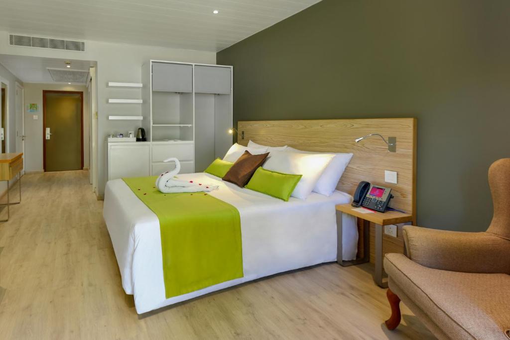 Mūsdienīga viesnīcas numura iekārtojums ar ērtu gultu, zaļu palagu un dekoratīvu gulbja izveidi. Numurā ir arī koka mēbeles, telefons un plaša uzglabāšanas telpa.