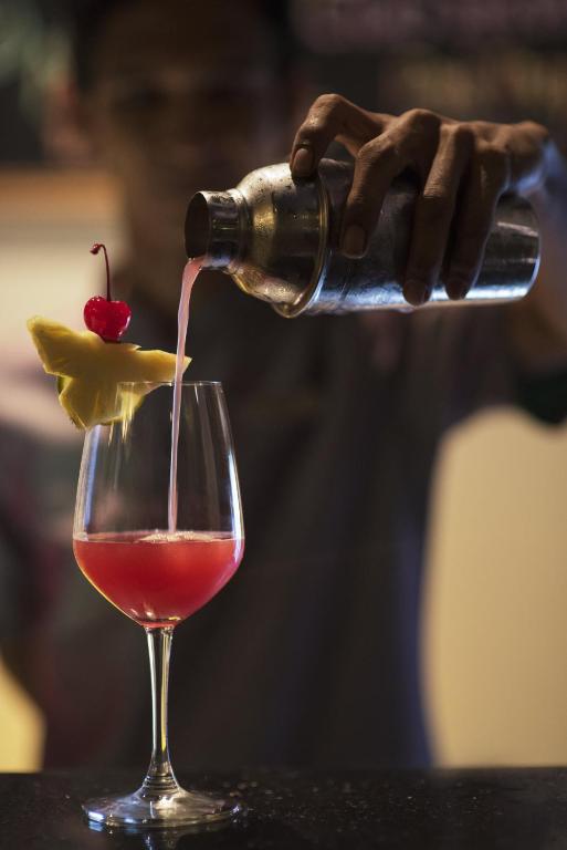 Kokteilis ar ananāsu un ķirsīšu dekorāciju tiek pasniegts, kamēr bārmenis to ielej no šejkera.