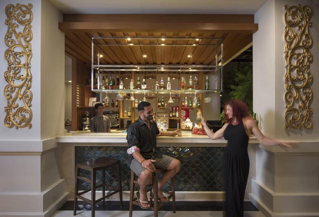 Elegants bārs ar diviem apmeklētājiem, kas izbauda kopā pavadītu laiku, kamēr bārmenis strādā fonā. Bāra plauktā redzami dažādi dzērieni un skaista interjera detaļas.