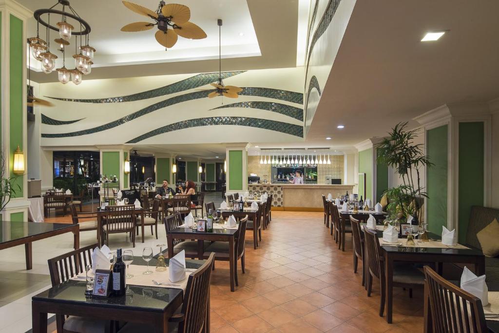 Restorāna interjers ar elegantiem galdiem un krēsliem, modernām lampām un zaļām sienām, radot patīkamu atmosfēru. Redzama bāra zona un apmeklētāji, kas izbauda maltīti.