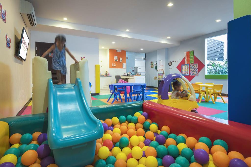 Bērnu rotaļu istaba ar slidkalniņu un krāsainām bumbiņām. Divi bērni izbauda spēles, viens slidinās, bet otrs spēlējas ar mašīnu.