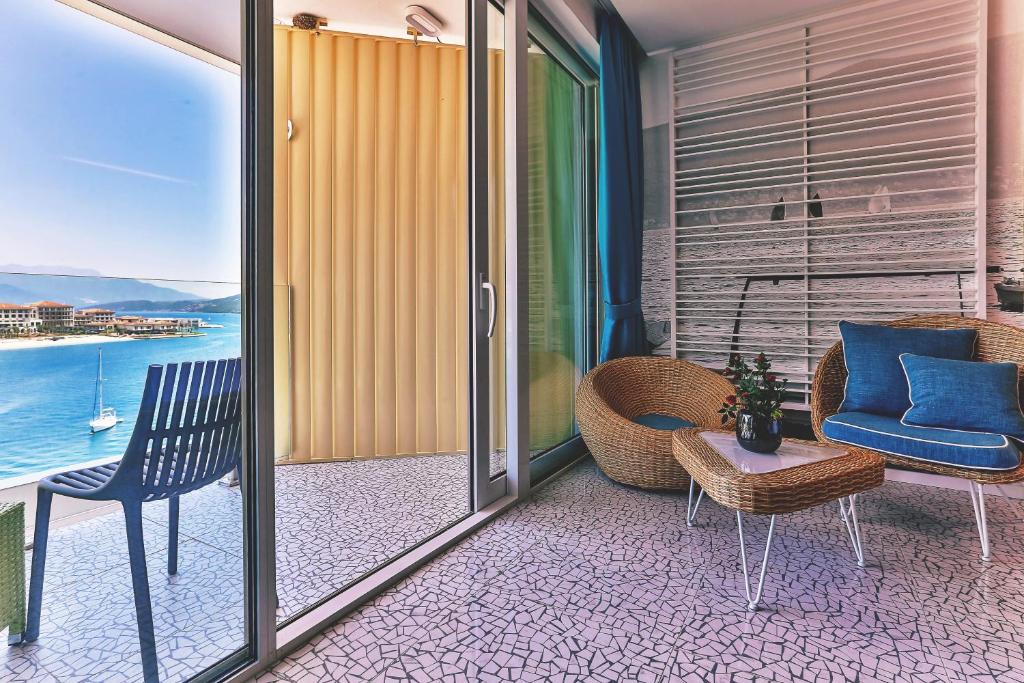 Balkona interjers ar skatu uz jūru, iekārtots ar vīna krāsas mēbelēm un zilu dīvānu, radot relaksējošu atmosfēru. Gaismas un krāsu harmonija piešķir telpai modernu izskatu.