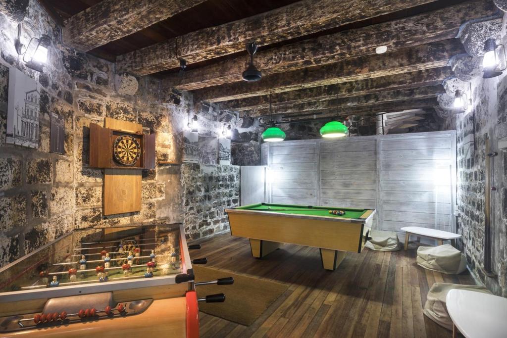Mūsdienīga atpūtas telpa ar galda futbolu, biljardu un šautriņu mērīšanu, dekorēta ar akmens sienām un koka sijām, radot siltu un mājīgu atmosfēru.
