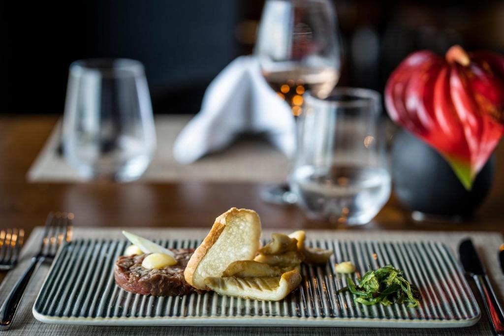 Gurmanu plāksne ar izsmalcinātu ēdienu, ieskaitot gaļas tartaru, ceptus dārzeņus un zaļumus, pasniegta eleganti iekārtotā restorānā.