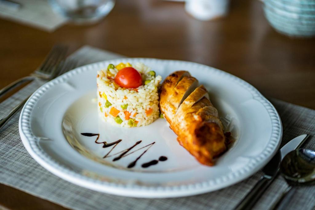 Skaisti pasniegta maltīte, kurā redzams rīsu salāti ar dārzeņiem un tomātu, kā arī cepts vistas gabals uz baltas šķīvja.