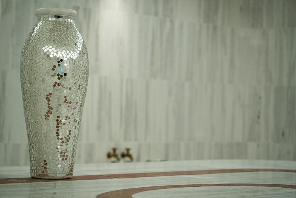 Mirdzoša mozaīkas vāze modernā interjerā, kas papildina telpas eleganci. Fons ar gaišu akmens apdari akcentē vāzes dizainu.